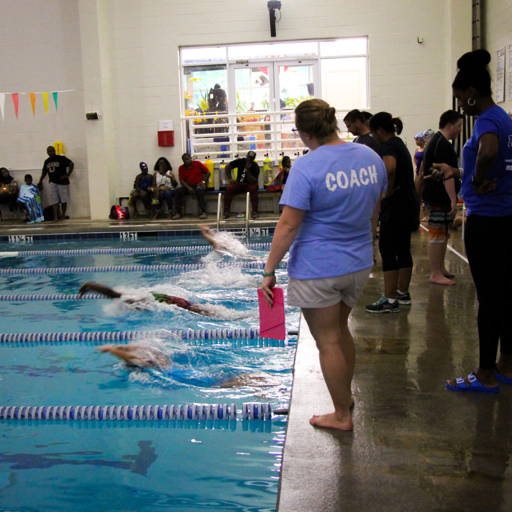 A swim coach is watching as 4 swimmers take their backstroke start during a swim meet.