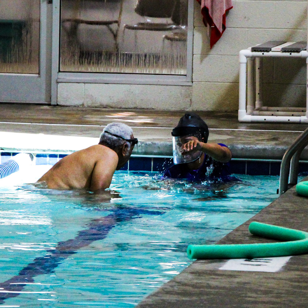 An adult swim student is watching his instructor demo the freestyle stroke with his arms.